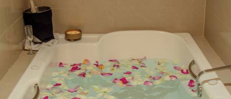 Una bañera llena de agua y pétalos de rosa, una vela y un vaso de agua al lado.