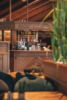 Uma área de bar com vigas de madeira, prateleiras repletas de garrafas, uma máquina de café e um balcão.