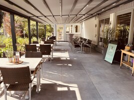 An outdoor patio area with tables and chairs, a signboard, and potted plants.