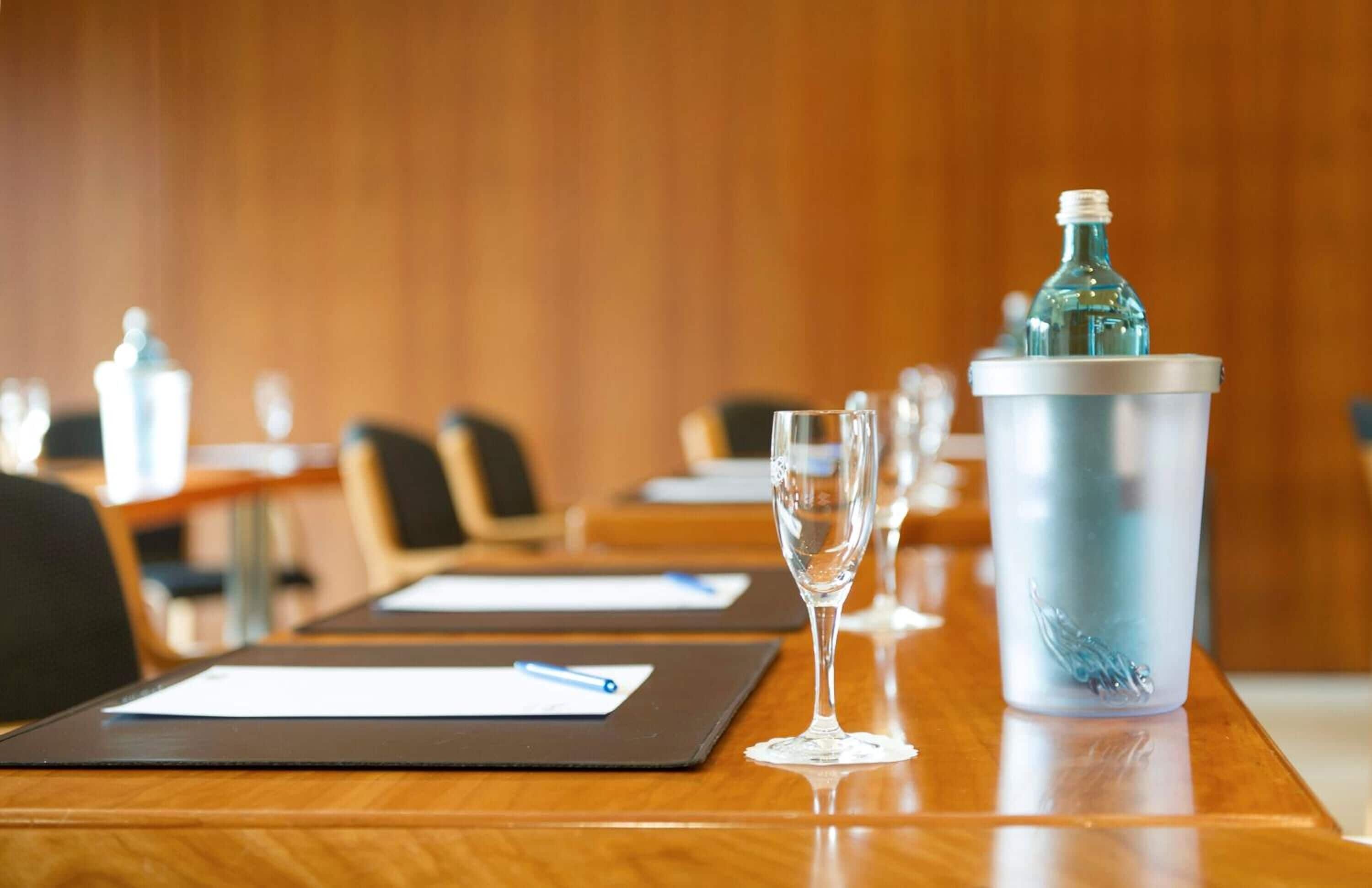 A conference room with a wooden table, a glass tumbler, and a metal tumbler with a bottle.