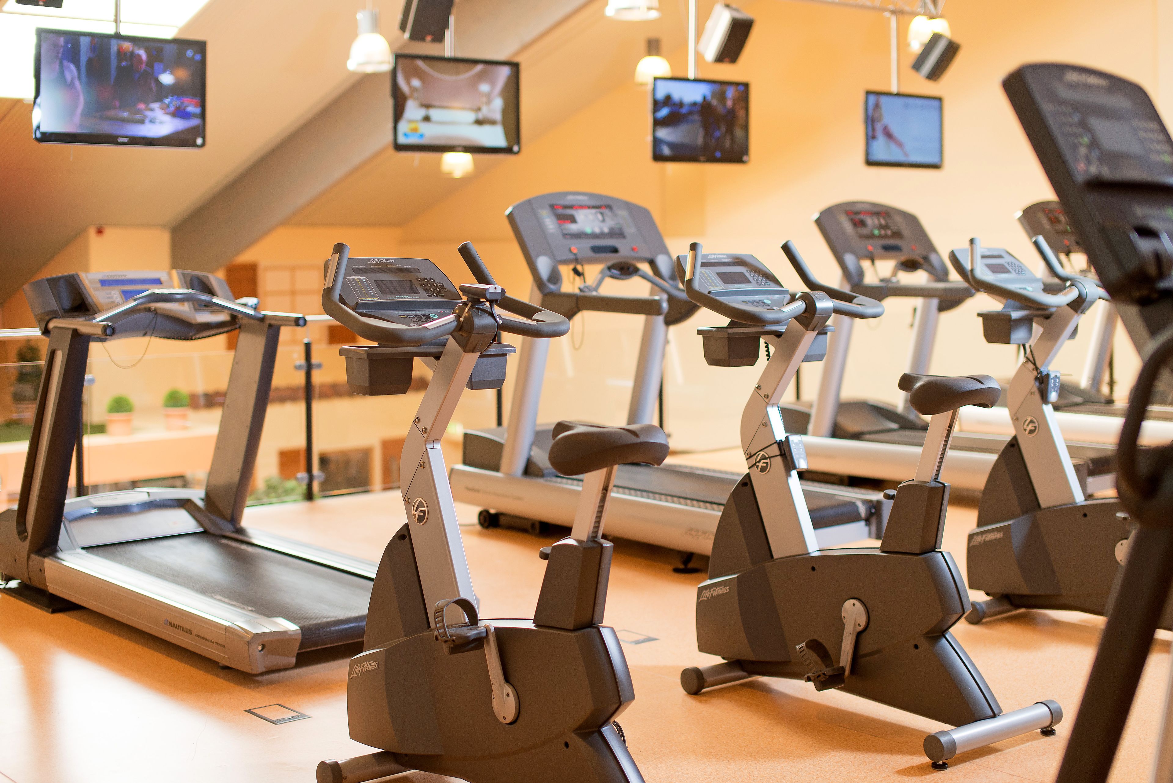 A row of stationary bikes in a gym with multiple screens on the wall.
