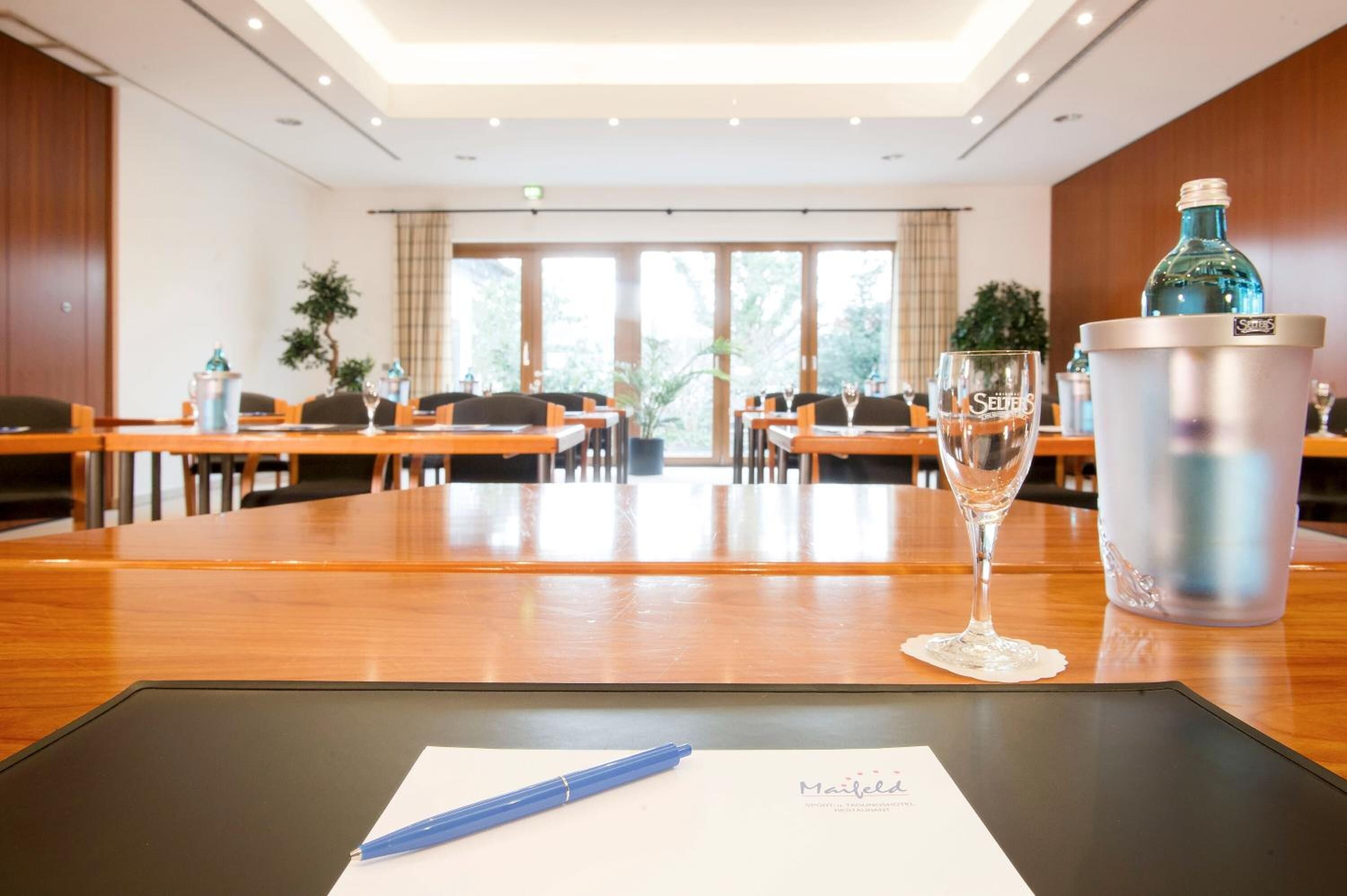 A conference room with a long table, chairs, a glass of water, a pen, and a menu on a black mat.