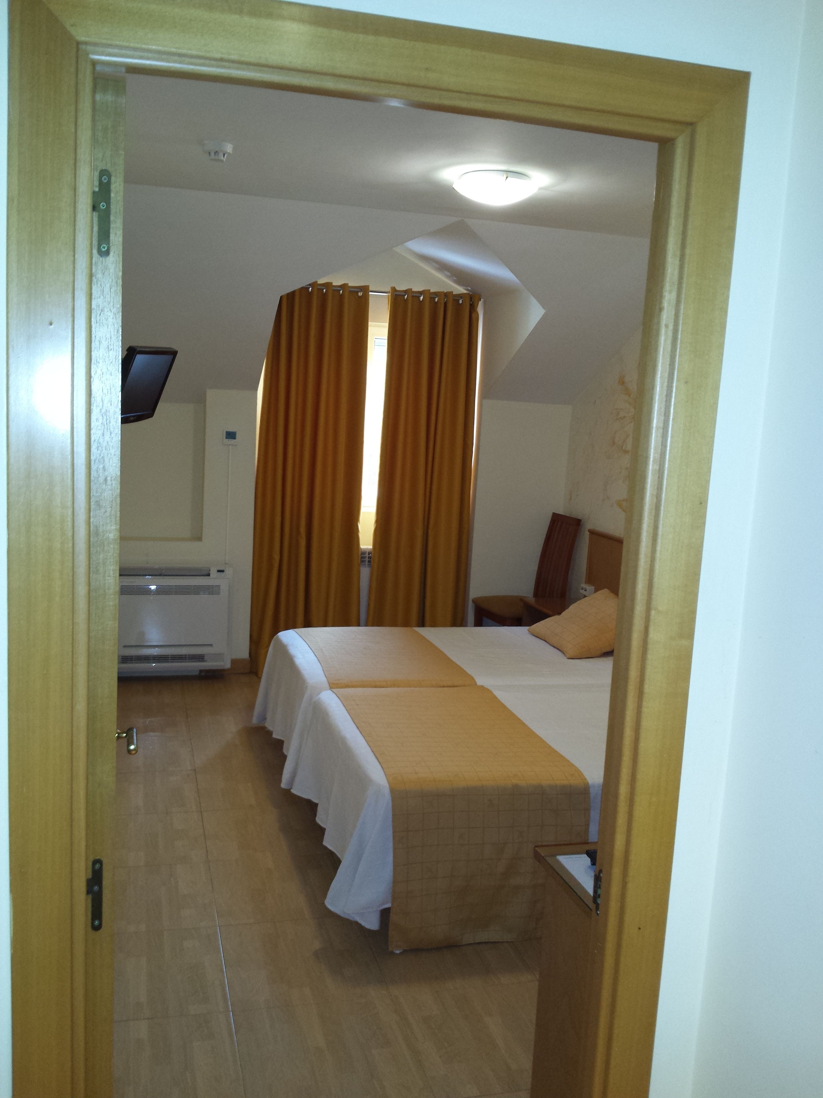 A hotel room with two beds, a desk, and an air conditioning unit.