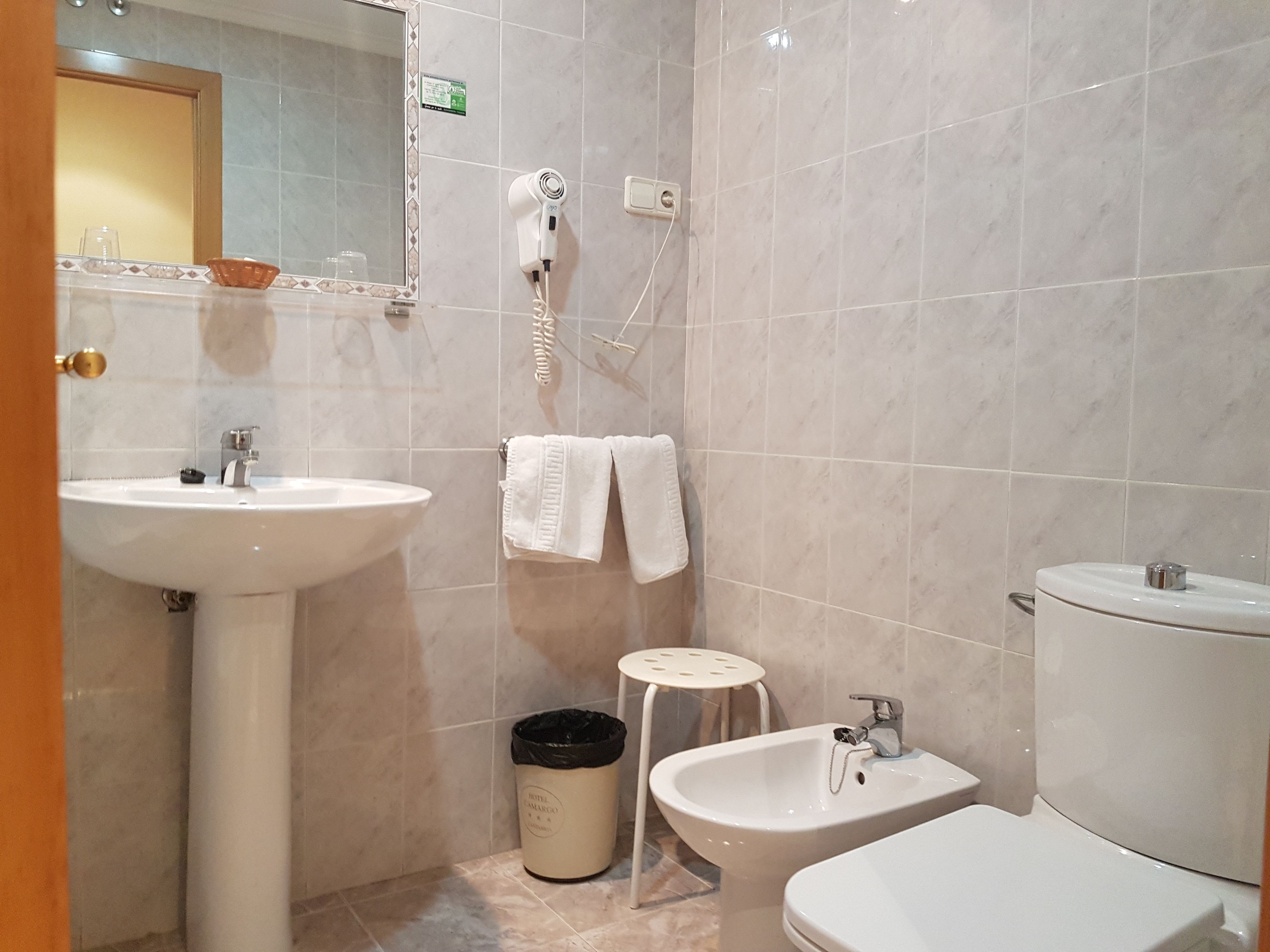 A bathroom with a sink, bidet, toilet, and a hairdryer on the wall.