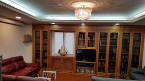 Ein Wohnzimmer mit einem roten Ledersofa, einem grauen Sofa, einem Fernseher und einem Bücherregal voller Bücher.