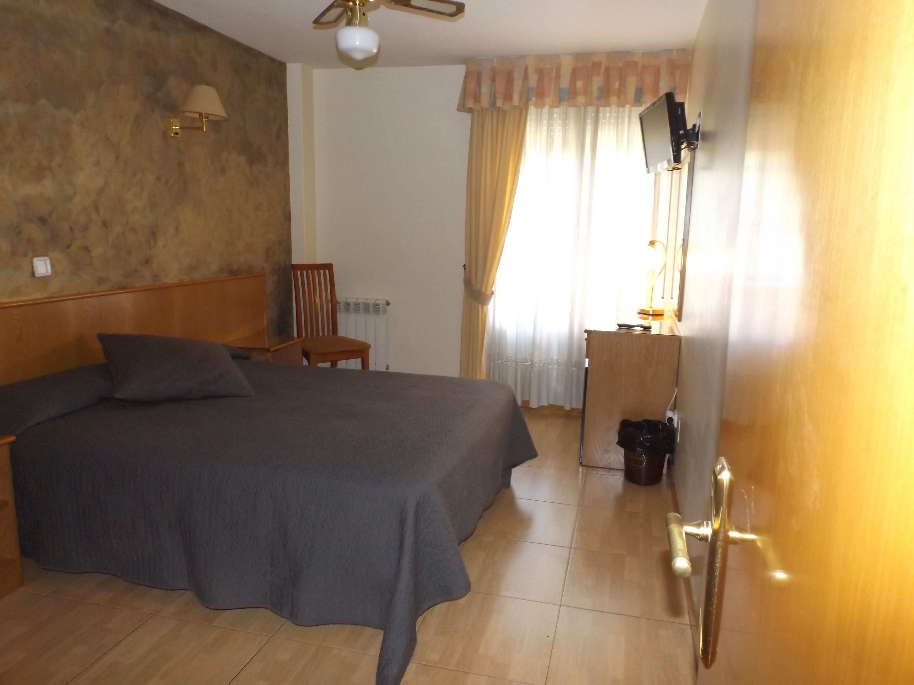 Una habitación de hotel con cama, una silla, un escritorio, un televisor y un radiador.