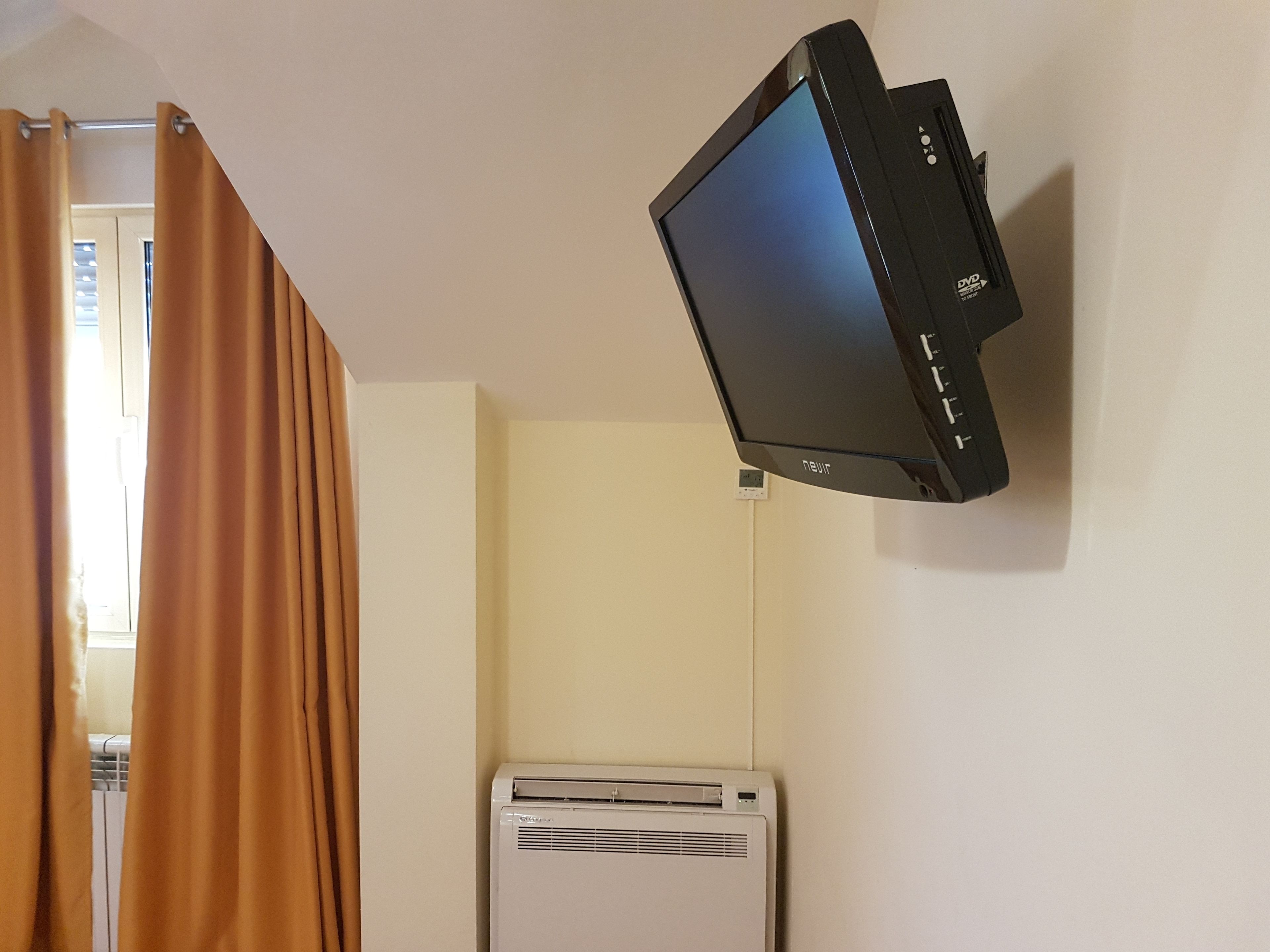 Une pièce équipée d’un téléviseur fixé au mur, d’un climatiseur et d’un rideau.