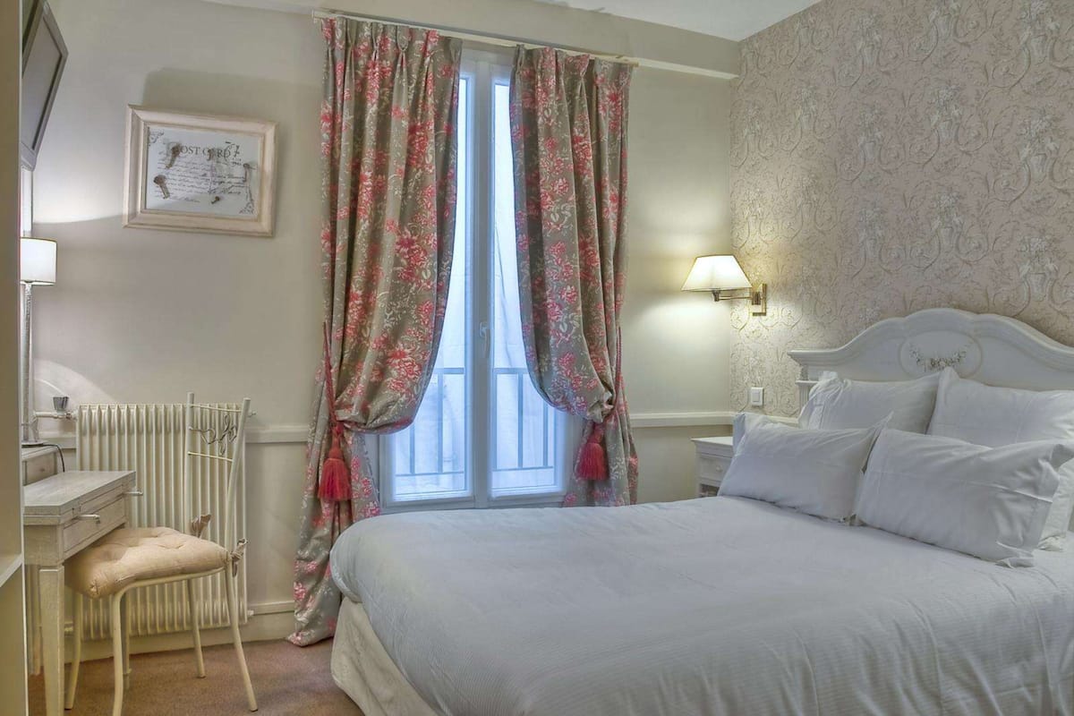 Een slaapkamer met een bed, een bureau, een stoel, een radiator en een raam met gordijnen.