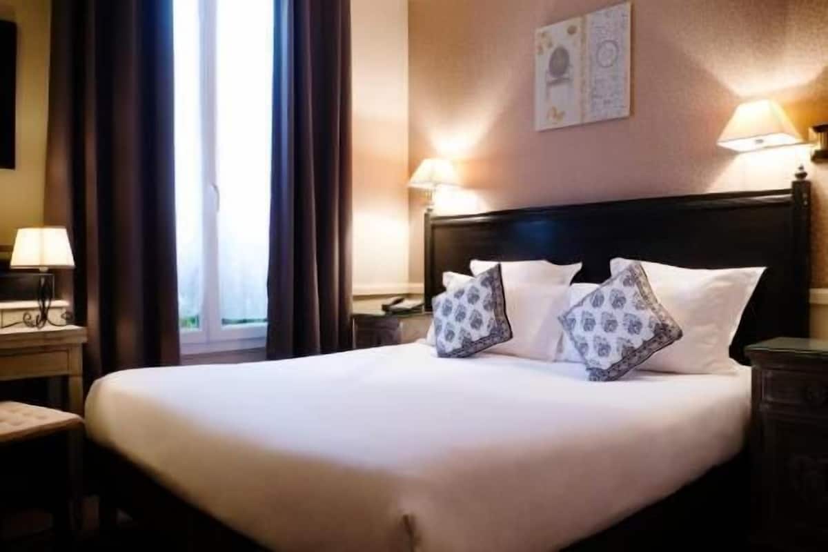 Een hotelkamer met een groot bed, twee bedlampen, een nachtkastje en een raam met gordijnen.