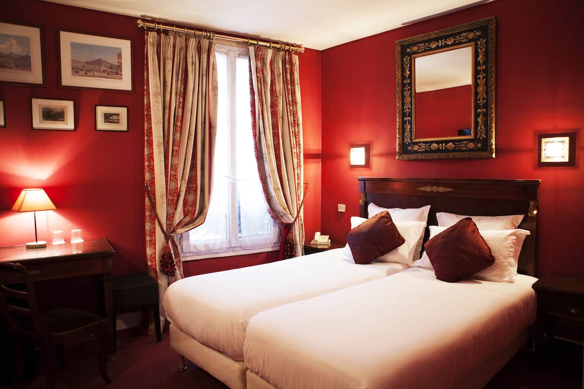 Een hotelkamer met een groot bed, een bureau met lamp en een raam met gordijnen.
