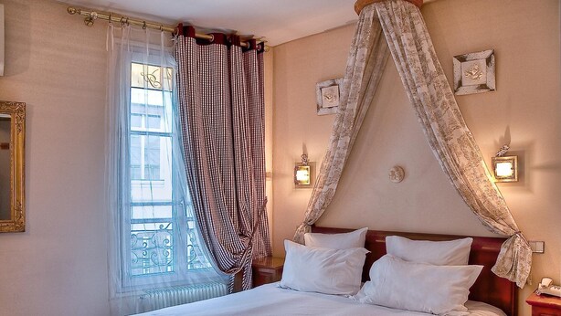 Una cama bien hecha con sábanas blancas, una ventana con cortina decorativa e iluminación en la pared.