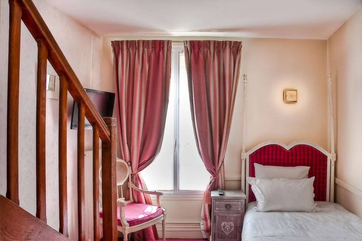 Een slaapkamer met een bed, een nachtkastje, een stoel en een raam met gordijnen.