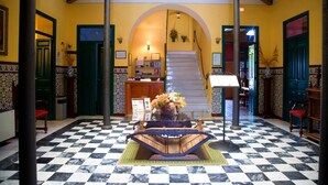 Un suelo a cuadros, una escalera y un mostrador de recepción en un edificio con paredes amarillas y puertas verdes.