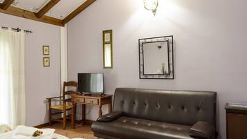Una habitación con un sofá de cuero marrón, un escritorio de madera con televisor, una silla y una cama con colcha estampada.