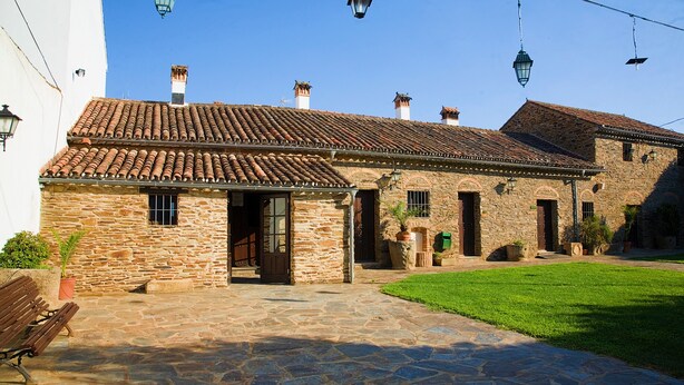 Un edificio de piedra con techo de tejas, un patio de piedra y un área con césped.