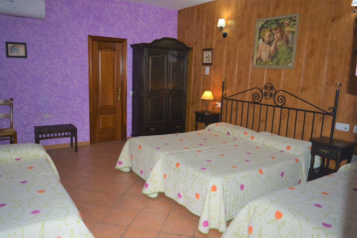 A bedroom with two beds, a wooden wardrobe, a bench, and a wall-mounted lamp.