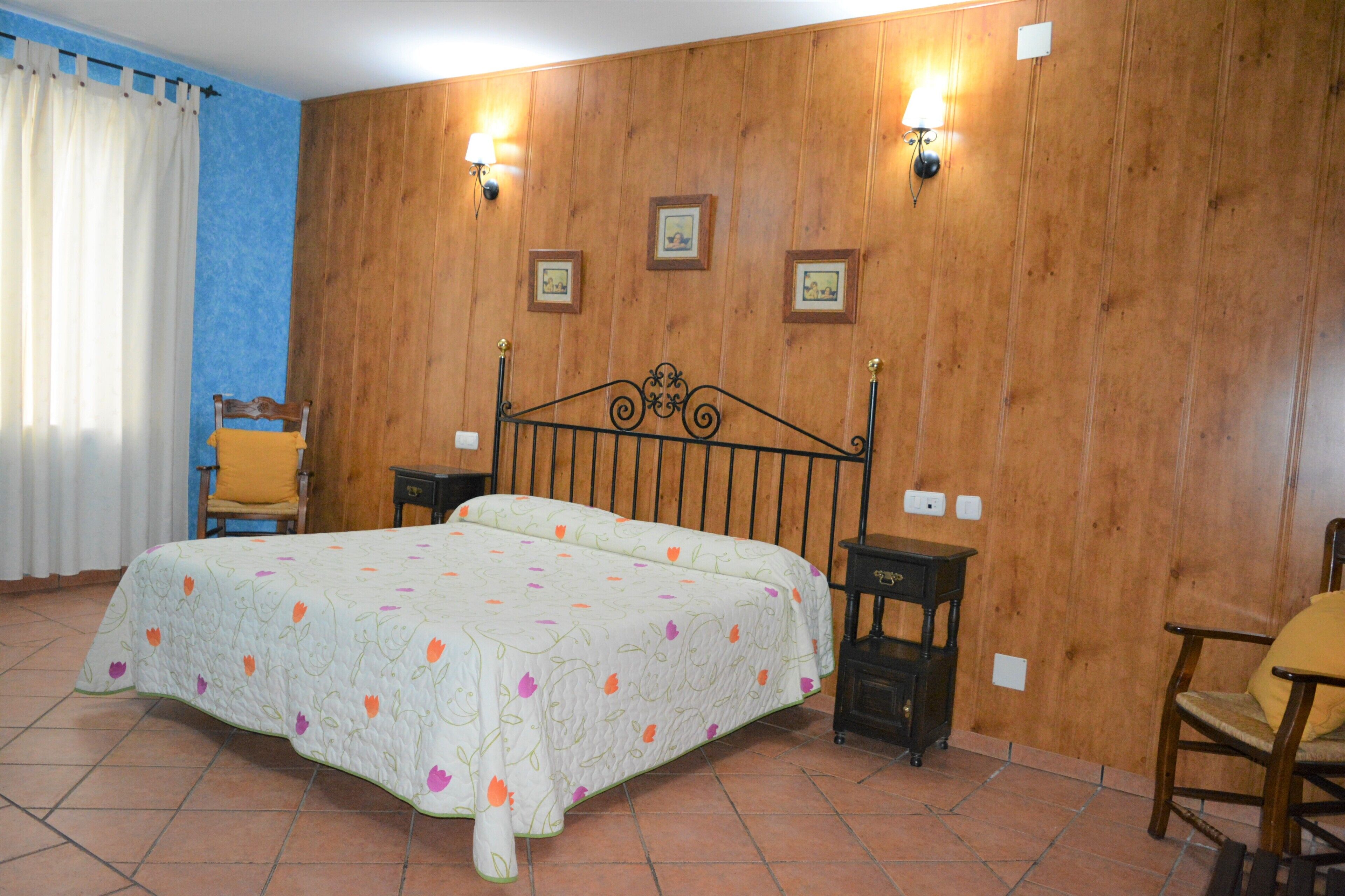 A bedroom with a bed, two nightstands, a chair, and a wooden wall with framed pictures.