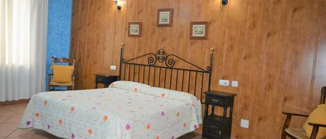 A bedroom with a bed, two nightstands, a chair, and a wooden wall with framed pictures.