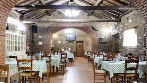 Un restaurante con paredes de piedra, vigas de madera y manteles a cuadros. Las mesas están dispuestas en filas con sillas.