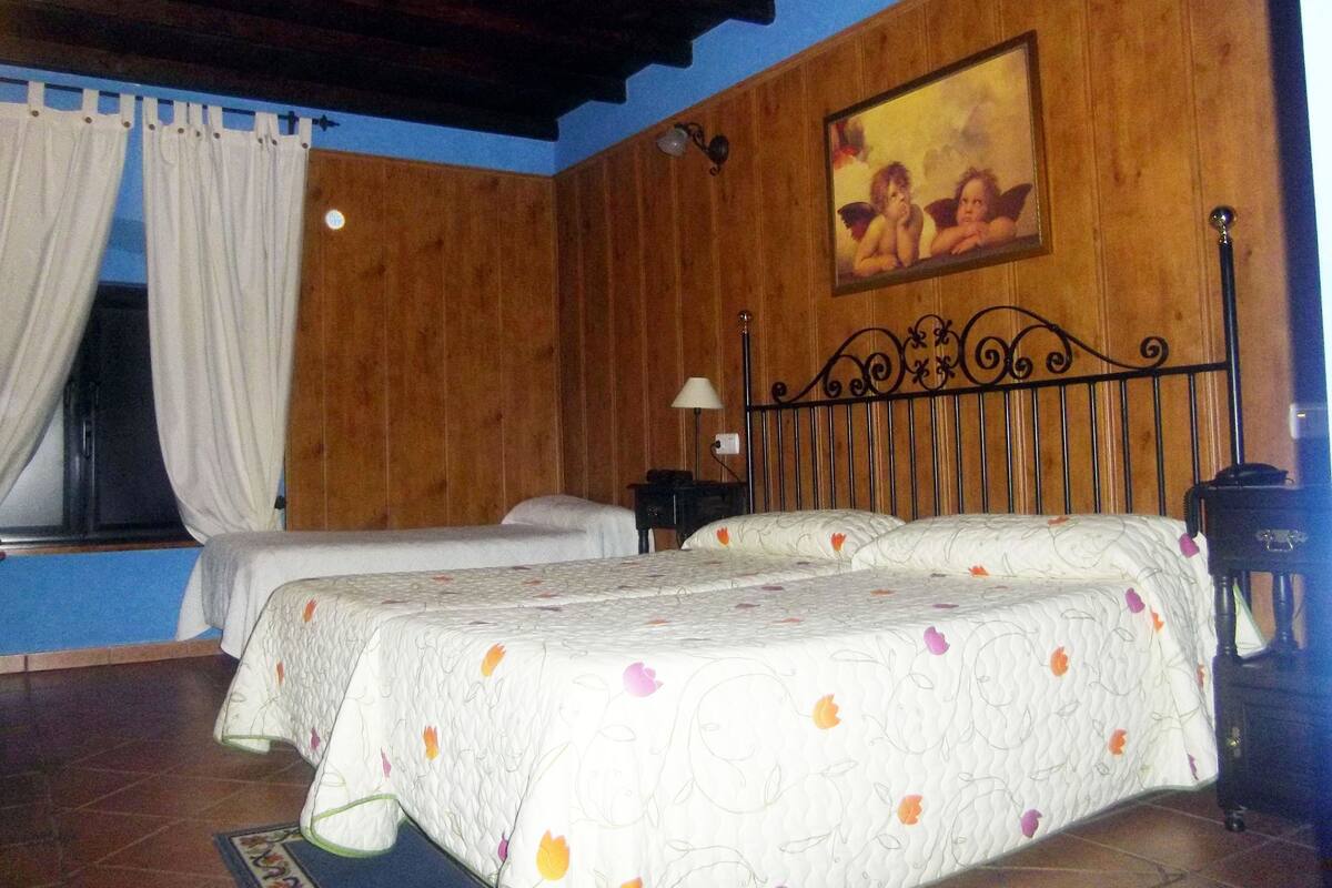 A bedroom with two beds, wooden walls, a painting, and a window with curtains.