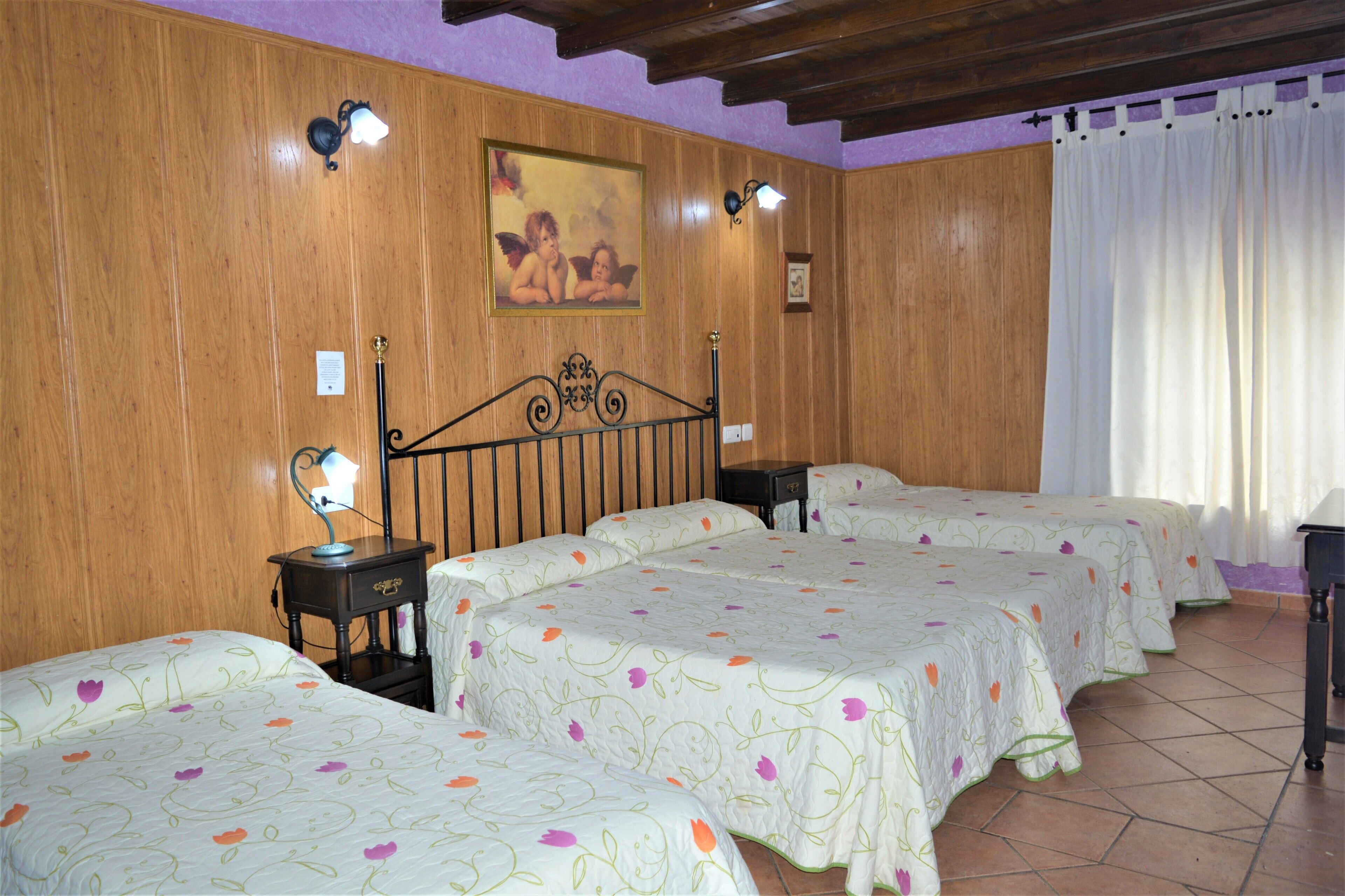 A hotel room with four beds, wooden paneling on the walls, a painting above the beds, and a tiled floor.