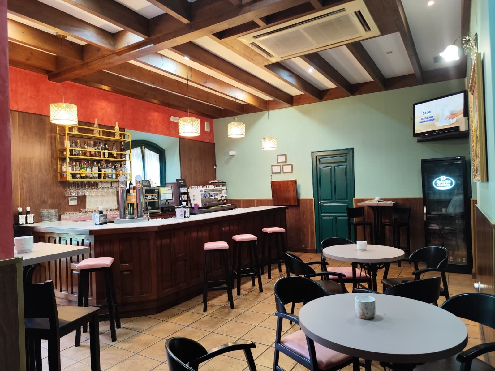 A restaurant with a bar area, multiple seating options including round tables and bar stools, and a television mounted on the wall.