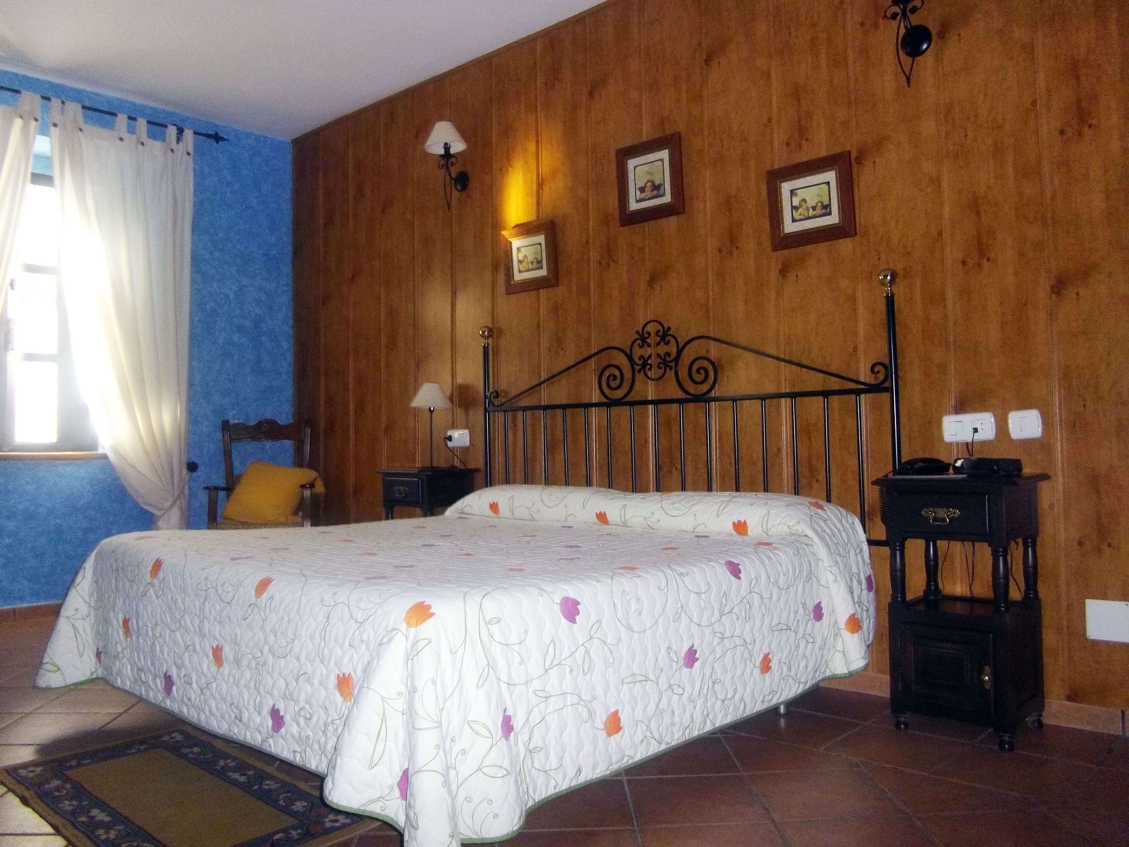 Un dormitorio con cama, mesitas de noche, lámpara y una pared de madera con cuadros.