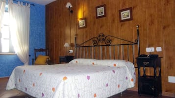Un dormitorio con cama, mesitas de noche, lámpara y una pared de madera con cuadros.