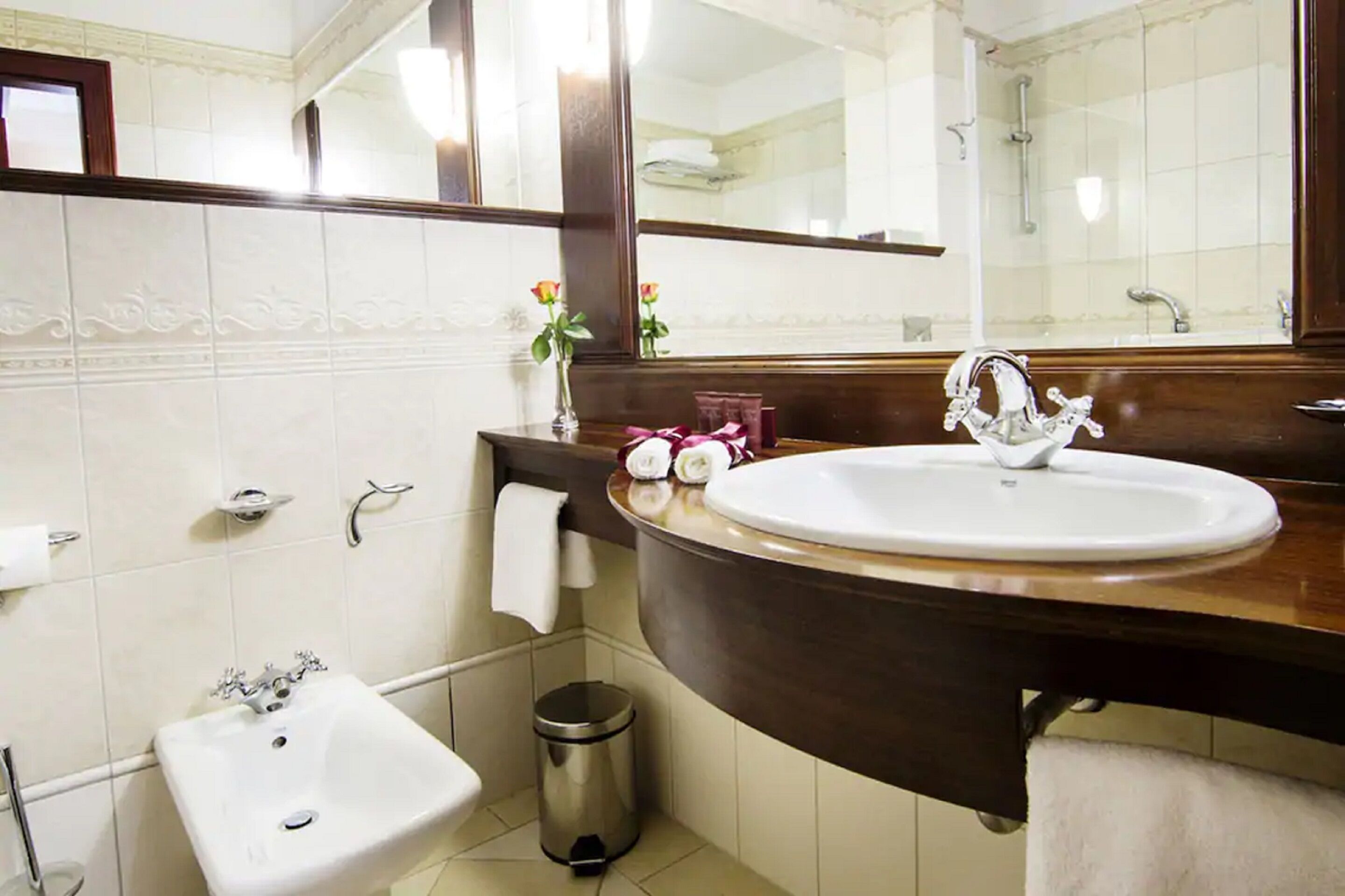A bathroom with a white sink, a mirror, a vanity with a dark countertop, and a small trash can.