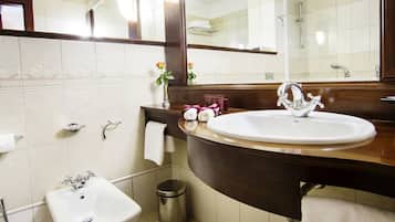 A bathroom with a white sink, a mirror, a vanity with a dark countertop, and a small trash can.