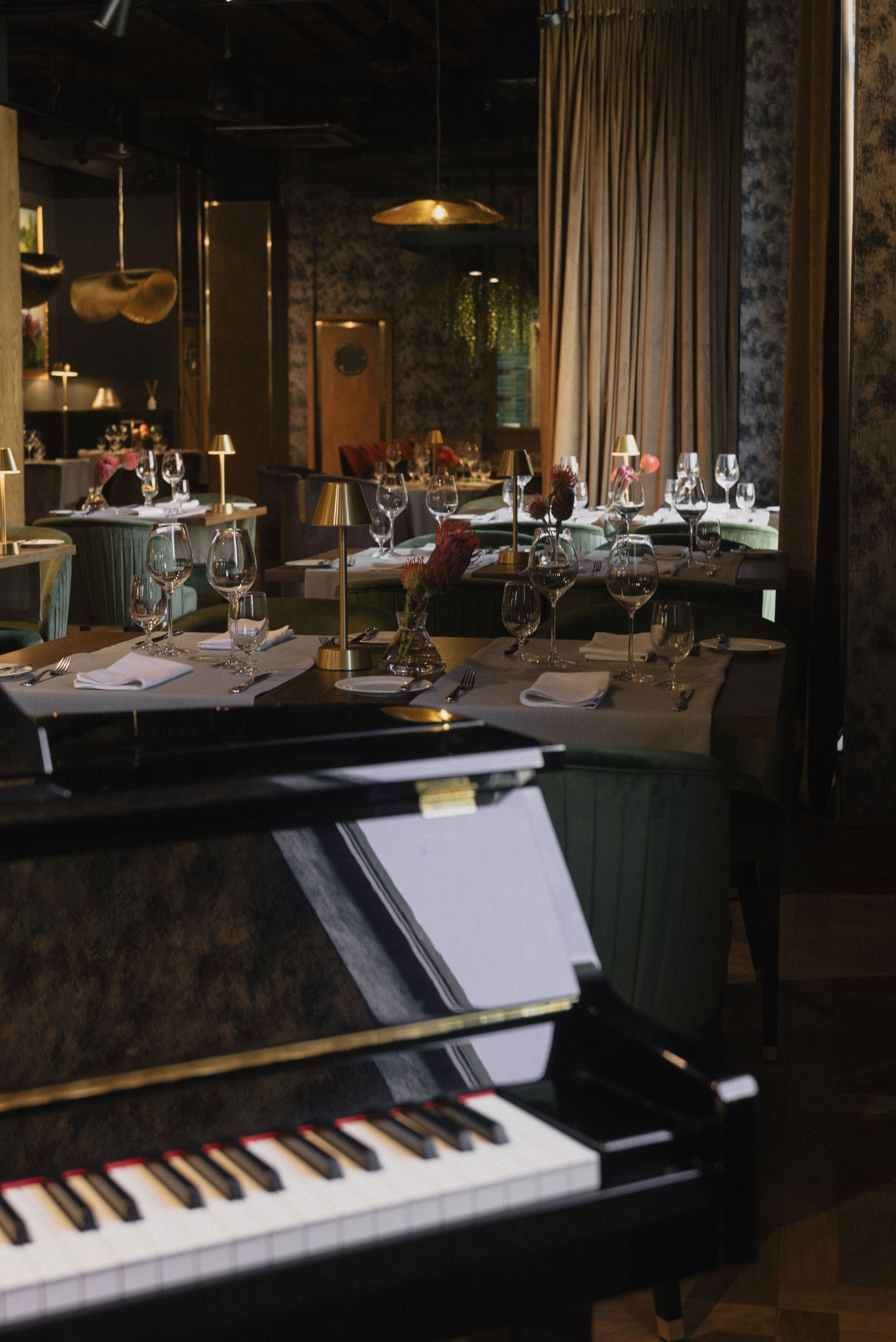 A dining area with tables set for a meal, a piano in the foreground, and a curtain in the background.