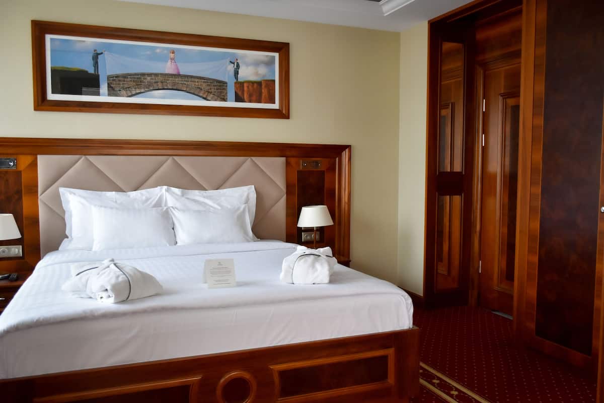 A neatly made bed with white linens, a headboard, and a framed picture above it.