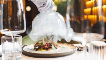 A waiter pouring a hot beverage over a dish, steam rising from the cup.
