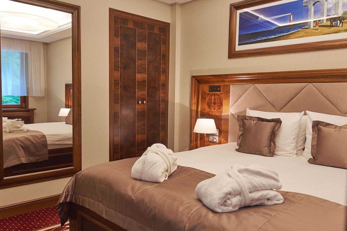 A hotel room with a large mirror, a bed with brown bedding, a headboard, and a painting above the bed.