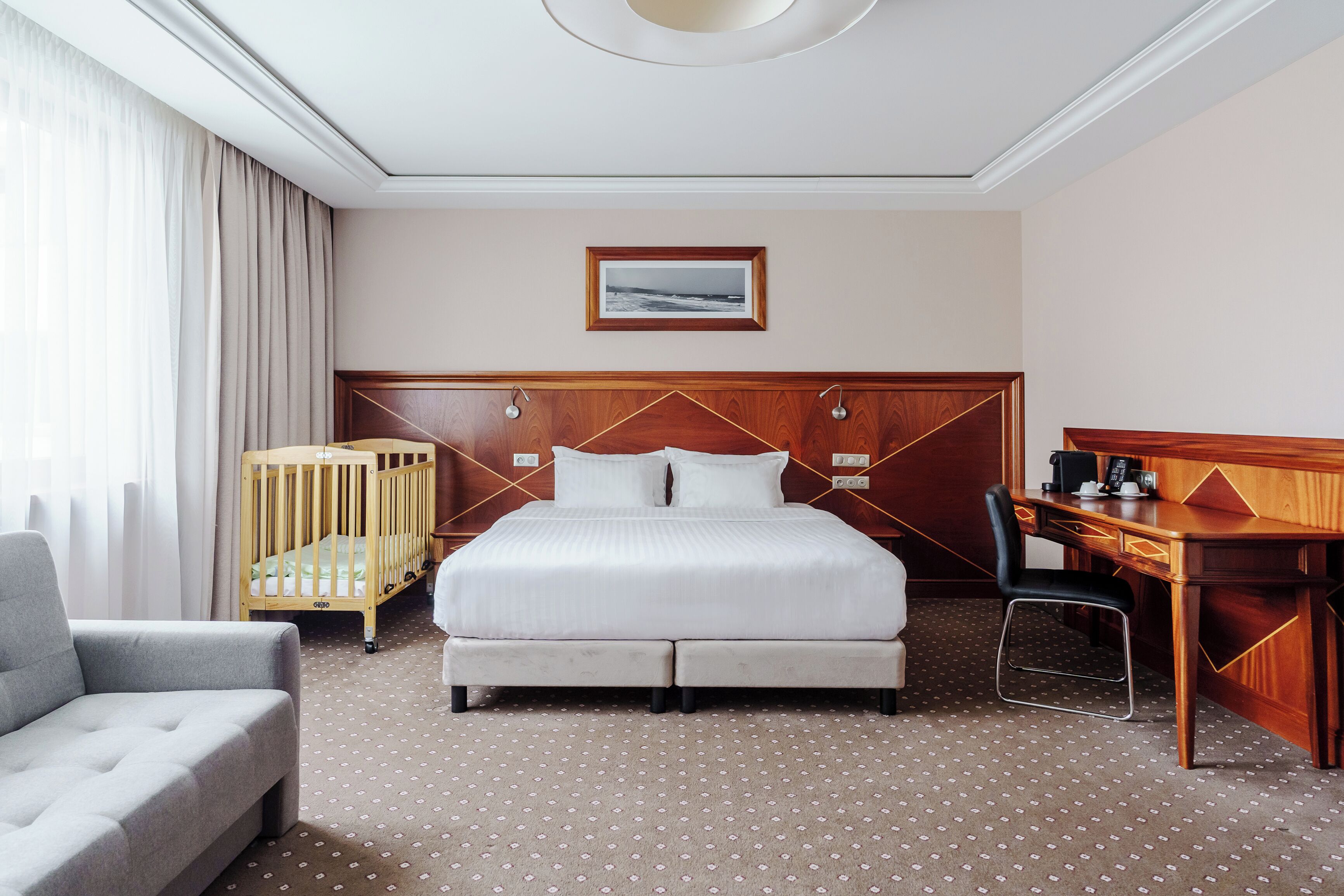 A hotel room with a bed, a desk, a chair, a crib, and a sofa.