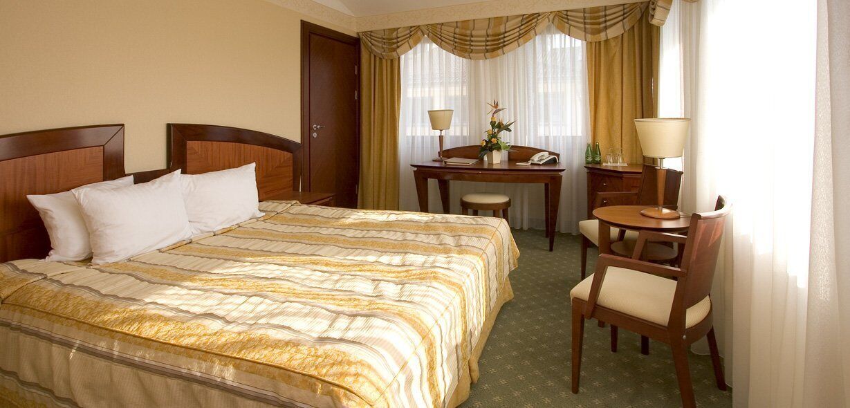 Una habitación de hotel con una cama grande, un escritorio con silla y una mesita con lámpara.