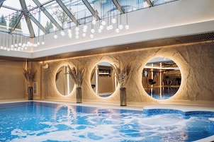 Una piscina interior con techo de cristal, ventanas circulares y diseño de techo de madera.