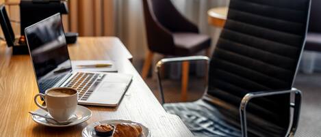 A wooden table with a laptop, a cup of coffee, and a plate with a croissant.