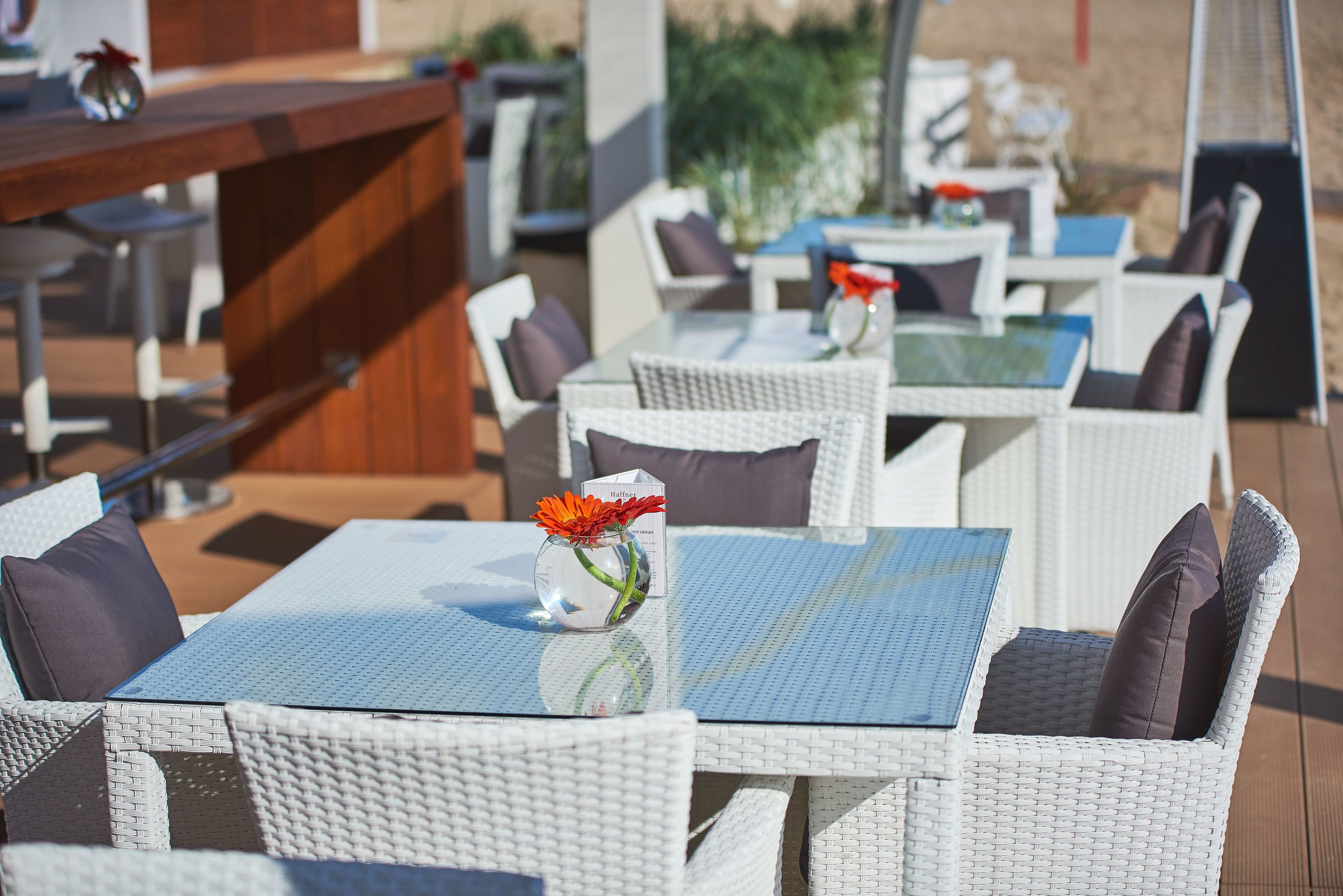 Outdoor wicker furniture with a glass table and a vase with a flower.
