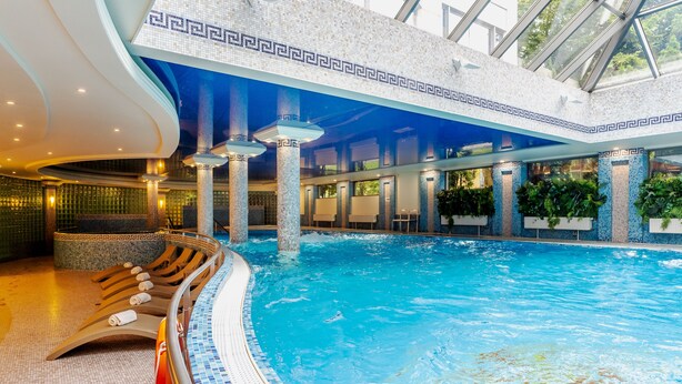 An indoor swimming pool with clear blue water, tiled walls, and a modern design with columns and seating areas. - Hotel Haffner Resort & SPA - Destigo Hotels (Sopot)