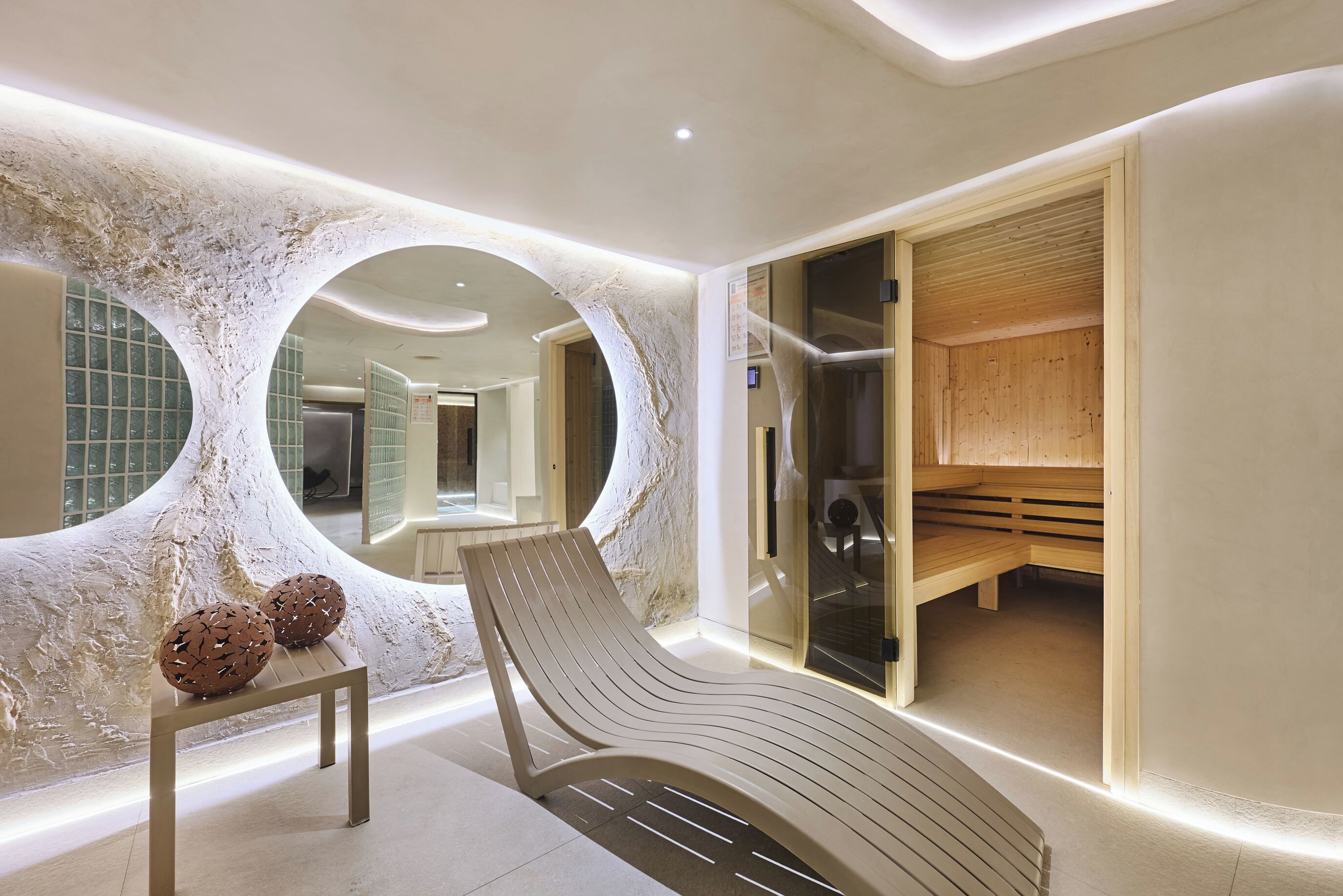 A modern spa room with a curved bench, a small table, and a mirrored wall.