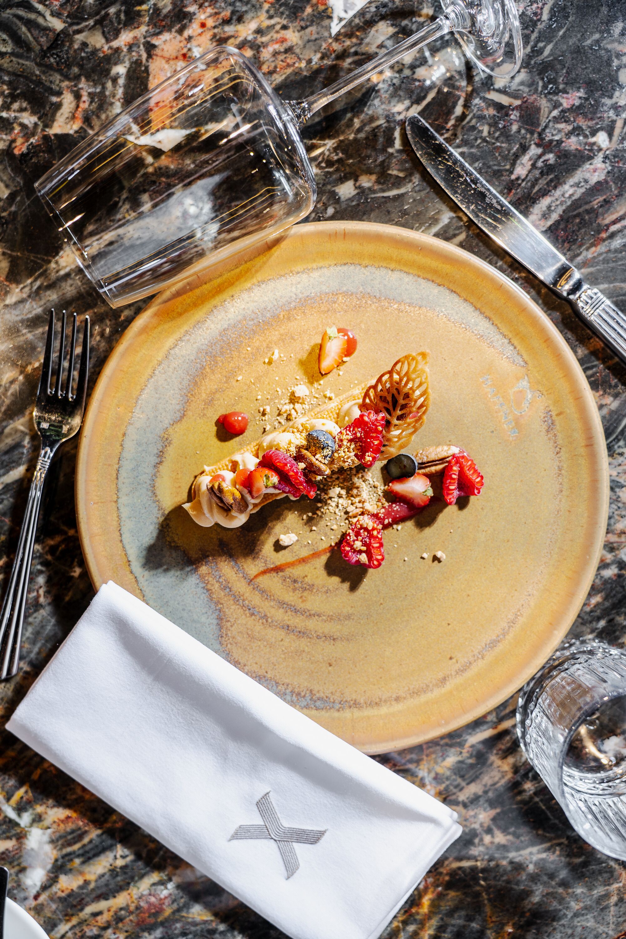 Un dessert présenté sur une assiette, accompagné d’une serviette et de couverts, le tout posé sur une surface en marbre.