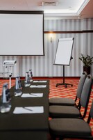 Una sala conferenze con un lungo tavolo, sedie, una lavagna, un proiettore e una pianta in vaso.
