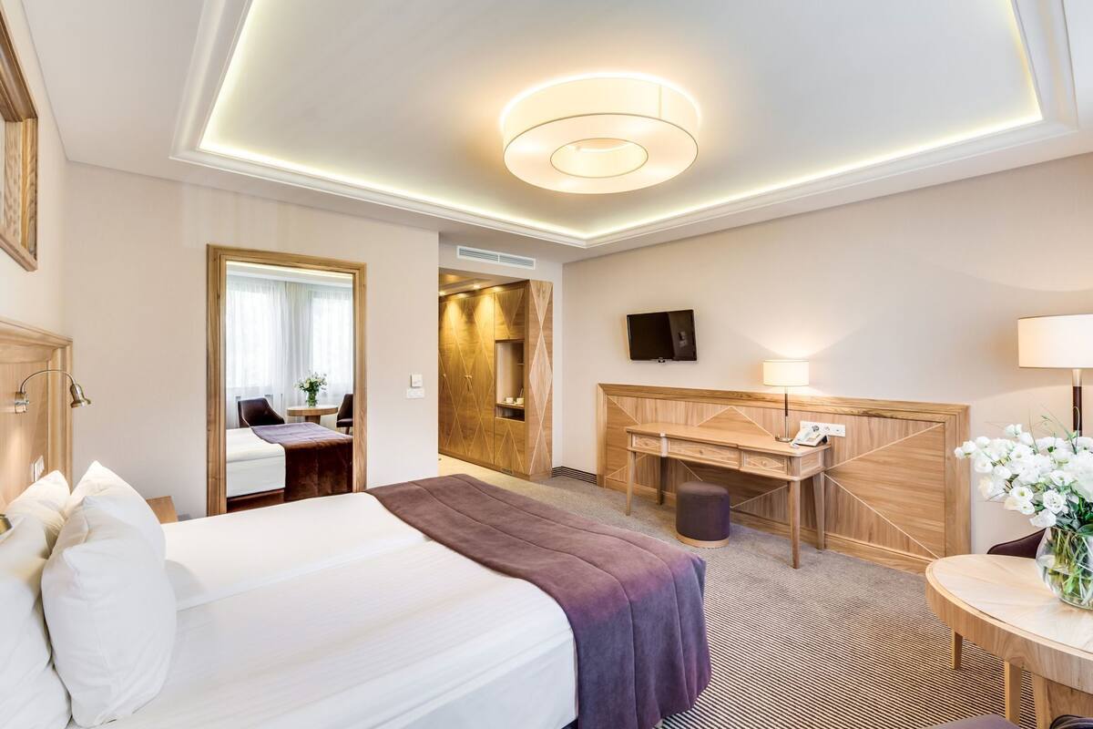 A hotel room with a bed, a desk, a television, and a bathroom visible through an open door.
