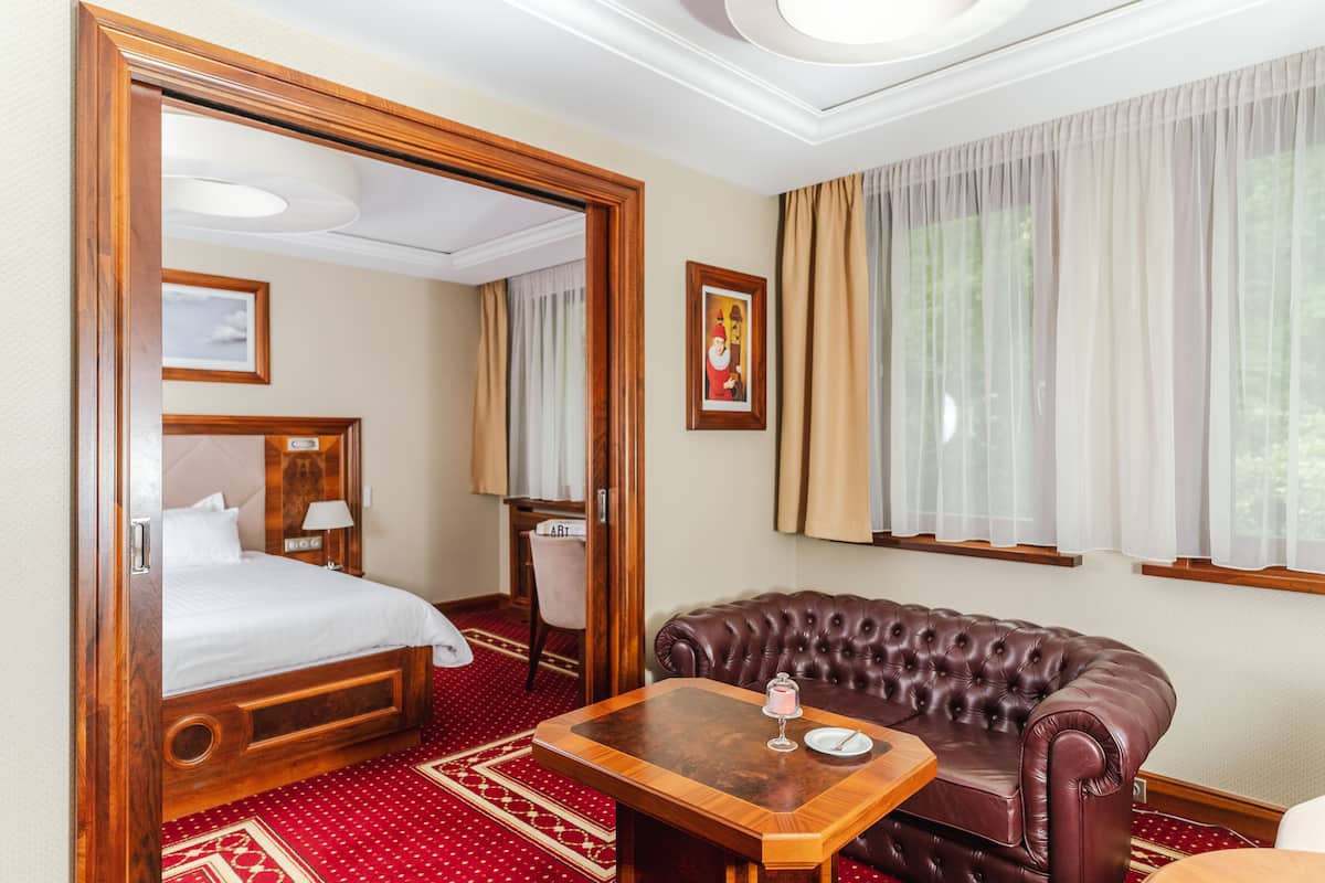 A hotel room with a bed, a leather sofa, a wooden table, and a large window with curtains.