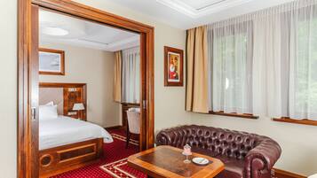 A hotel room with a bed, a leather sofa, a wooden table, and a large window with curtains.