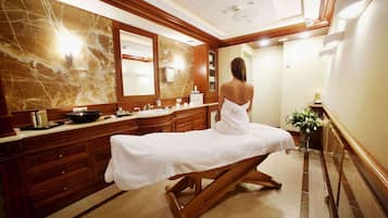 A spa room with a massage table, wooden cabinets, marble walls, and a large mirror.