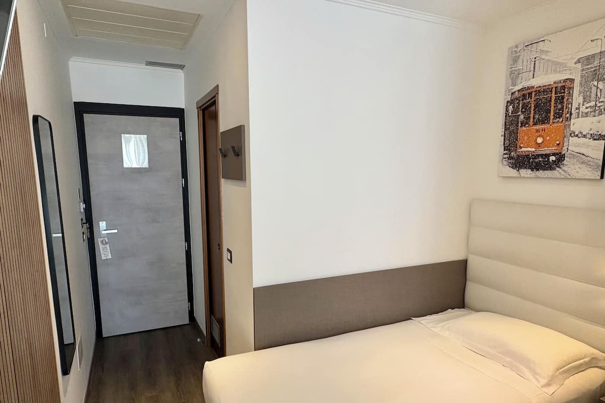 A hotel room with a bed, a door, and a wall-mounted picture.