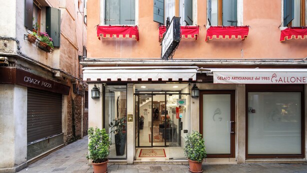 Un escaparate con persiana baja, plantas en macetas y un letrero que dice 'Crazy Pizza'.