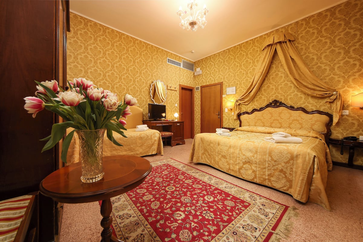 A hotel room with two beds, a TV, a desk, and a vase of flowers.